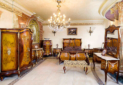 A charming and unique French Louis XV style ormolu-mounted double veneer and opulent floral marquetry inlaid eight pieces Bombe shaped Royal Bedroom Suite adorned with masterfully chiseled shells, ormolu trims, ribbon-tied swaging garlands extended with suspending swaging imbricated blossoming floral garlands and ormolu female busts to the corner of each piece within the set, the cabriole legs terminate with ormolu scrolling acanthus sabots; the rich set is comprising of one bed, one armoire, one dressing table with mirror, one coiffeuse, one commode, one semainier and two nightstands.