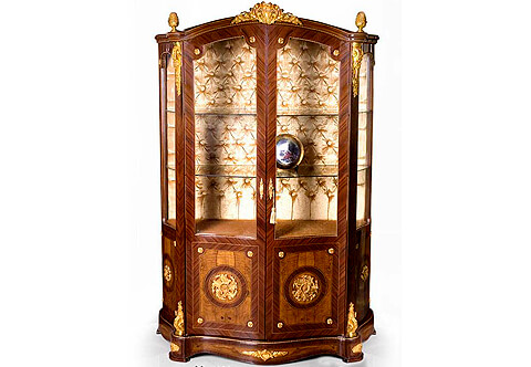A French Napoleon style ormolu-mounted veneer inlaid China Cabinet, The domed eared top crested with central ormolu mount and ormolu pine cones above two full size quarter sans traverse veneer inlaid doors, with glazed panels, ormolu rosettes, and ormolu keyhole escutcheons, With two glass shelves on a velvet upholstered tufted background, The lower part of the doors adorned with finely chiseled large flower rosettes ormolu mounts placed on waterfall bubinga veneer background within a circular palisander filet and opens to reveal one shelf inside, The corner supports ornamented with richly cast acanthus ormolu volute chutes on top and bottom above the ormolu mounted serpentine shaped plinth, The sides with glazed panels and similarly designed as the front, Luxurious vitrine, corner furniture, Serre Bijoux, Francois Linke-vitrine, jean-henri riesener vitrine, Leon Message vitrine, Francois Linke display cabinet, cabinet vitrine, Louis xv vitrine, Louis xvi vitrine, ormolu mounted vitrine, Louis XIV vitrine, display cabinet, vernis martin style vitrine, French style vitrine, glass vitrine, English style vitrine, veneer inlaid vitrine, marquetry vitrine, Italian style vitrine, glass round vitrine, boulle style vitrine, antique reproduction vitrine, antique style display cabinet, empire style bookcase vitrine, display cabinet with porcelain plaque, French style Vitrine, English Style Vitrine, Ormolu-mounted Vitrine, Louis XV style Vitrine, Vernis Martin style painted Vitrine, Antique style Vitrine, Antique style Glass Cabinet, Antique style Corner Vitrine, Andres Charles Boulle Vitrine, Carved Vitrine, Antique Display Bookcase, High Quality Antique Furniture Reproductions, Antique Furniture, antique furniture manufacturer in egypt, antique furniture gallery, antique furniture store