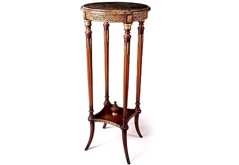 An astounding French early 19th century Louis XVI style ormolu-mounted circular tall Pedestal Table after the model by François Linke; Raised on splayed tapering legs followed up to four circular tapering fluted supports surmounted with two levels ormolu and wooden mottled caps above lovely fitted ormolu chandelles and terminated with other mottled caps, the lower section is connected with concaved sides X stretcher lower tier with a central topie shaped finial and embellished on sides with wonderful ormolu band of draped fabrics and tassels design with a beaded pattern top; The upper circular tier is surmounted with a mottled border circular marble top above a circular frieze decorated with stunning pierced foliate scrolled Rinceau shaped ormolu movements of richly chased acanthus leaves and separated above each support with wooden block accented with rectangular ormolu rosette.