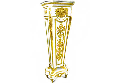A prepossessing French late 19th century Louis XVI style ormolu-mounted and highly finished white lacquered Grand Royal Pedestal after the model by the famous German ébéniste (cabinetmaker) Jean-Henri Riesener; surmounted by a stepped white carrara marble top and canted front corners above an Egg-and-Dart ormolu trim, on a rectangular concave upper section followed and centered by a Mercury sunburst ormolu mask with crossed lower branches, the angles with an acanthus-cast scrolled volute hung and foliate festoons, above the tapering upright, the paneled front finely chiseled and burnished with a flower-filled Rinceau style vase ormolu pattern flanked by scrolling foliage and floral swags issuing suspending festoons above a Lyre and crossing blowing instruments with surrounding wreath, all placed within an ormolu beaded trim, on winged lion-paw feet and shaped plinth on toupie leafy feet.