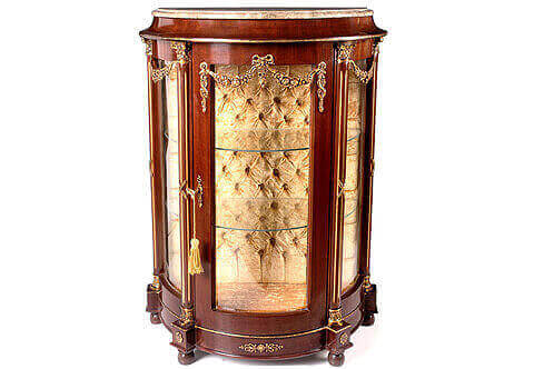 Demilune shape French Neoclassical style ormolu-mounted Cabinet-Vitrin, surmounted by a shaped marble top and ornamented with ormolu ribbon-tied floral blossoming garlands and flanked to the four corners by gilt-fluted columns supports with an ormolu Corinthian capitals and resting on ball feet. Available per request with upholstered tufted back or mirror back as displayed