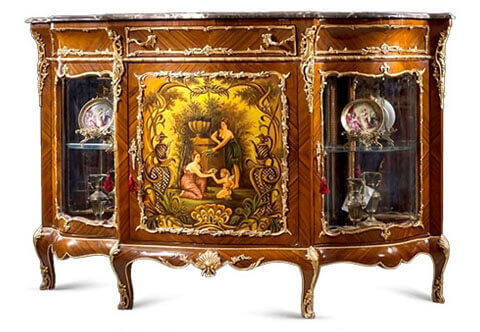 A luxuriant Napoléon III gilt-ormolu mounted veneer inlaid and Vernis Martin serpentine shaped side display cabinet, after the model by Henri Picard Circa 1880, Marble topped, The central door decorated with a fine painted cartouche with classically dressed nymphs giving water to cupid by a well, The vernis -Martin technique became popular again in the later years of the 19th century. Patented by Guillaume and Simon-Etienne Martin in 1748, it was developed to imitate Far Eastern, particularly Japanese, lacquerware, The process uses copal and amber varnishes which are layered onto the desired surface.  The varnish is then polished with pumice powder and sealed with oil to create a smooth, glossy finish, Many 19th century painters added a craquelure to the varnish to imitate the original varnish of the Martin brothers as seen over 100 years earlier