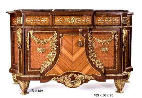 Magnificent Napoleon III ormolu-mounted veneered commode after the model of Jean-Henri Riesener, circa 1783, with a breakfront beveled marble top, above an entwined foliate-cast frieze set with three drawers and centered with the monogram MA for Marie-Antoinette, above a central gilt-bordered inlaid two doors with keyhole escutcheon and two ormolu cabushon handles, flanked by suspended floral swaging garlands with large fine chiseld and burnished ormolu foliate chutes above a shaped apron ornamented with Cyma Recta brass trim and centered with a floral wreath and flanking cornucopiae, each raised on tapering acanthus-sheathed feet, extraordinary in finishing and details