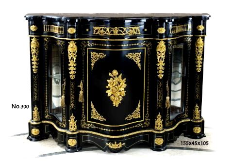 A Napoleon III gilt-ormolu mounted ebonized side cabinet of serpentine outline, inlaid overall with foliate strapworks and acanthus scrolls, marble topped above a conforming frieze with central drawer ornamented with ormolu acanthus scrolls and ormolu pulls flanked by curved sides ornate with ormolu galleries separated by flower rosettes on a curved blocks, all above a central door ornamented with fine chiseled gilt-ormolu flower bouquet cornered with ormolu scrolling foliage within an ormolu border and hand gilt decoration with a fine ormolu keyhole escutcheon, a large fine chiseled and burnished acanthus and palmettes chutes to each side and flanked by shaped glass doors sided with the same ormolu espagnolette, all on a scalloped shaped plinth with the same ormolu works and gilt patterns