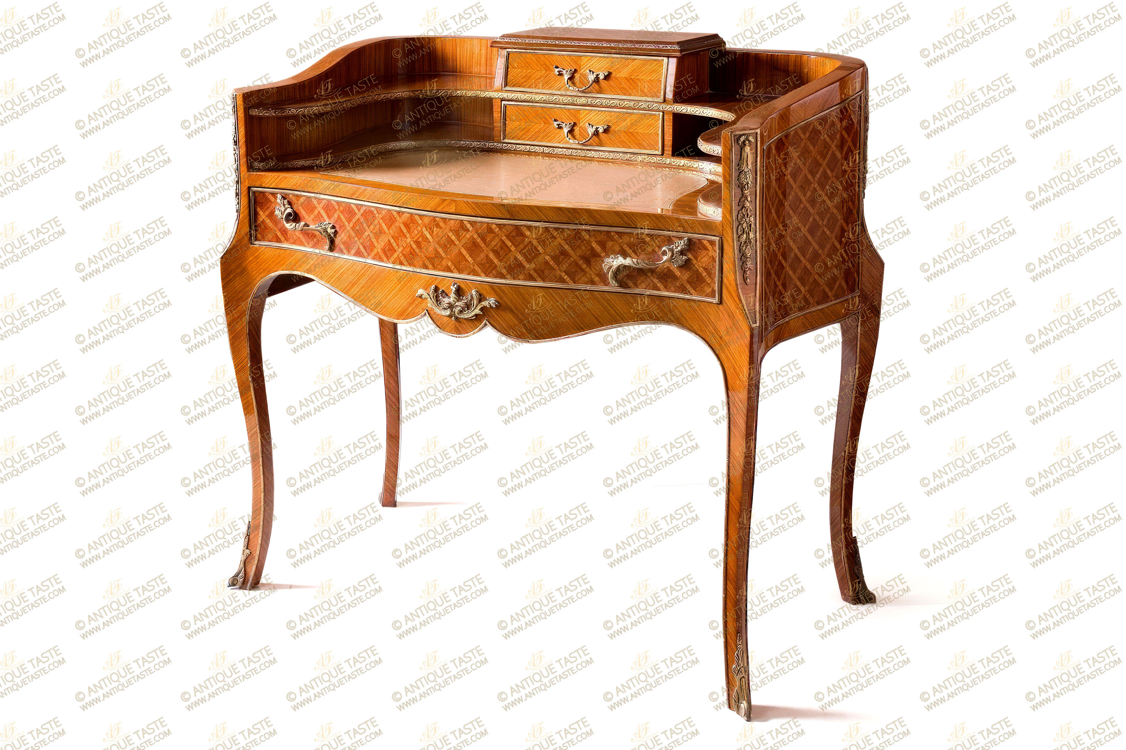 An aesthetic and most delicate French Napoleon III Transitional style ormolu-mounted trellis parquetry and sans-traverse veneer inlaid Bonheur Du Jour Bureau De Dame | Ladies Secretary Desk; The curve-shaped two shelves back ornamented with a hammered ormolu band centered with two small drawers decorated with a gilt-ormolu strip to the front and drape ormolu band the back, upholstered inside in dark red velvet fabric, surmounted with a beveled top inlaid with an ormolu strip; Above is an inset gilt-tooled leather writing surface above a scalloped shaped frieze with a central foliate ormolu mount and housing a wide drawer, upholstered inside in dark red velvet fabric and decorated with two ormolu foliate handles and framed with an ormolu band; The sides, the back and the central wide drawer are inlaid in parquetry style within an ormolu strip. The lower contour of the bureau is bordered with an ormolu filet; The concave-shaped corners with foliage ormolu mounts within an ormolu band, raised on slender splayed cabriole legs terminated with foliate scrolled ormolu sabots.