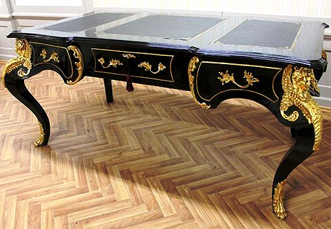 A grandiose French Louis XV style ormolu-mounted black color partner bureau plat on the manner of Andre Charles Boulle, The shaped eared top with three sectional gilt-tooled leather writing surfaces above scalloped frieze with three drawers have foliate ormolu handles and bordered with hammered ormolu borders, The central drawer with ormolu foliate keyhole escutcheon and separated from the side drawers with elegant C shaped ormolu floral gadroons, Raised on a robust cabriole legs surmounted with ormolu winged caryatids on acanthus-sheathed, The tapering cabriole legs terminate with ormolu leafy paw sabots, The scalloped shaped sides framed with fine chiseled floral strip centered with a fine chiseled satin and burnish finished Satyr mask, The back with three faux drawers same to the front