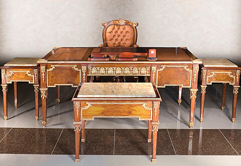 An Opulent Continental 18th century Louis XVI style crouch mahogany and ormolu-mounted executive desk, The desk is raised on eight square tapered legs each with ormolu top detailed festoon pendants headed with a hammered wrap around ormolu trim and terminating with wrap around ormolu acorn finial sabots. The long vertical block above each long adorned with fine square rosette issuing imbricated laurel pendants, At each side are four drawers, 'sans traverse', displaying the warm and fine crouch mahogany grain continuing from one drawer to the other, Each set of two framed within a fine chiseled ormolu border with C scrolls connections and swaging drapes shaped handle to each one, At the recessed apron is a central drawer decorated with a sensational and high quality satin and burnished finished pierced acanthus leaves chain band ormolu mount above a beveled ormolu trim and an ormolu keyhole escutcheon, At each side panel are fine repeat mahogany panels displaying the warm grain and framed within the same ormolu band and C scrolls connections, Above, framed in an ormolu gallery is the gilt tooled fitted leather writing surface with four foliate ormolu clasps to each corner. Three sectional leather top surface in another version. The back is identically decorated with no drawers, The desk is available in a set includes three tables of an identical design of the desk with a marble top