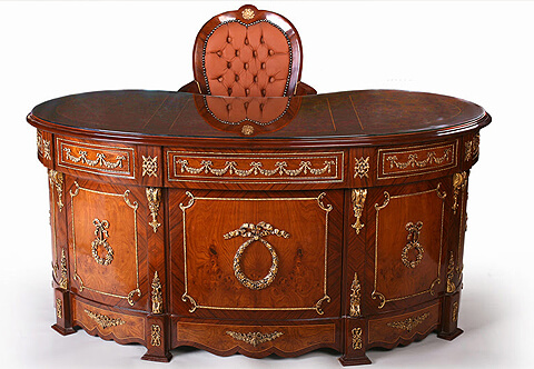A graceful French Neoclassical style mahogany and veneer inlaid ormolu-mounted kidney shaped executive desk, The veneer inlaid filet sectional moulded kidney shaped top above three drawers ornamented with ormolu festoons, ormolu trims and lyre shaped handles, separated by blocks ornamented with ormolu rosettes, above two deep drawers to each side framed with ormolu trim connected with foliate C scrolls and scrolled ormolu handles, The four side supports flanking the drawers ornate with ormolu Ancone of Bracket, all above a scalloped shaped plinth with blocks and faux drawers decorated with Neoclassical style ormolu mounts, The back side has the same design all over, the central three sections ornamented with ormolu knotted ribbons and circular laurel wreath and ribbon tied laurel hanging tassels