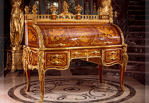 Our elaborate copy of the marvelous Bureau Du Roi ( Secrétaire Cylindre de Louis XV), The King Desk, the most celebrated piece of 18th century French furniture after the model by Jean-François Oeben and Jean-Henri Riesener, The fine piece is manufactured of the solid beech wood and covered with intricate marquetry and veneer inlays of a wide variety of fine woods and fine chiseled gilt ormolu mounts, The open ormolu pierced gallery top surmounted with ormolu urns of prosperity, ormolu female busts with acanthus foliate movements and two celebrating putti on acorn and scroll-works to the center, The rectangular top gallery is bordered with beaded leaf and dart on cyma reversa ormolu band surrounding marquetry works, The beautiful cylinder roll up inlayed with striking sans traverse veneer inlays centered with a flower bouquet flanked to both sides with marquetry of musical instruments and trophies all within a foliate scrolled veneer entwined filet, and two foliate ormolu handles, opens to reveal a marquetry and veneer inlaid substantial pullout sliding writing surface, smaller drawers and chambers of medium sizes, The curved sides of the desk are adorned with ormolu laurel leaves terminating with clasps and inlaid with marquetry patterns of foliate royal cartouche to the internal parts, the outer sides has the same marquetry works of the cylinder front, At the scalloped shaped frieze below is a central drawer with ormolu keyhole escutcheon flanked with two smaller drawers to each side framed with brass filets, all have foliate ormolu handles, foliate marquetry ornamentations and scrolled veneer fillets, bordered below with highly detailed foliate ormolu filets in a satin and burnish finish extending to the legs, At each corner are large and impressive ormolu mounts of richly chased royal male and female, fleur de lis and scroll works, repeated to back, The sides are professionally ornamented with highly detailed ormolu filets in a satin and burnish finish representing a central issuing festoons with knotted ribbon pendants to the sides, curving laurel bay leaf to the bottom centered with marquetry and acanthus marquetry, connected to a central shell issuing foliate filets topped with foliate marquetry and extending to internal side of the legs, The back has the same marquetry patterns of the front, the top part is centered with a large ormolu plaque of playful putti, The desk is raised on cabriole legs inlaid with foliate marquetry inlays and terminating with turned acanthus ormolu cast sabots