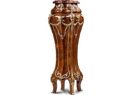 A breathtaking French Napoleon III Second Empire Louis XV Revival style ormolu-mounted and sans-traverse double veneer inlaid bombe shaped grand Vase Stand; The surmounting inset marble top fitted in a cornice adorned with ormolu foliage on each corner; above a sectioned bombe shaped curved body, the upper part is centered to each side with finely chiseled ormolu mounts of typical Empire style Egyptian female mask with an anthemion crown headdress issuing scrolling acanthus leaves flanked with pierced ormolu floral chutes to each corner elongated to second curved section of the body with ormolu chutes of winged human mask with pierced scrolled body and blossoming floral addendum extended with a hammered ormolu band to the lower part terminating with scrolling blossoming ormolu foliage and curved ormolu sabots ornamenting the cabriole robust legs; The body center is embellished on each side top with ormolu winged eagle as a symbol for freedom, strength, power and high purpose issuing blossoming floral swaging garlands connected to ormolu scrolling acanthus volute Rinceau and reversed Fleur de Lis plus ormolu hammered encadrements terminates in curved scrolls and connected with central ormolu mounts of scrolling foliage.