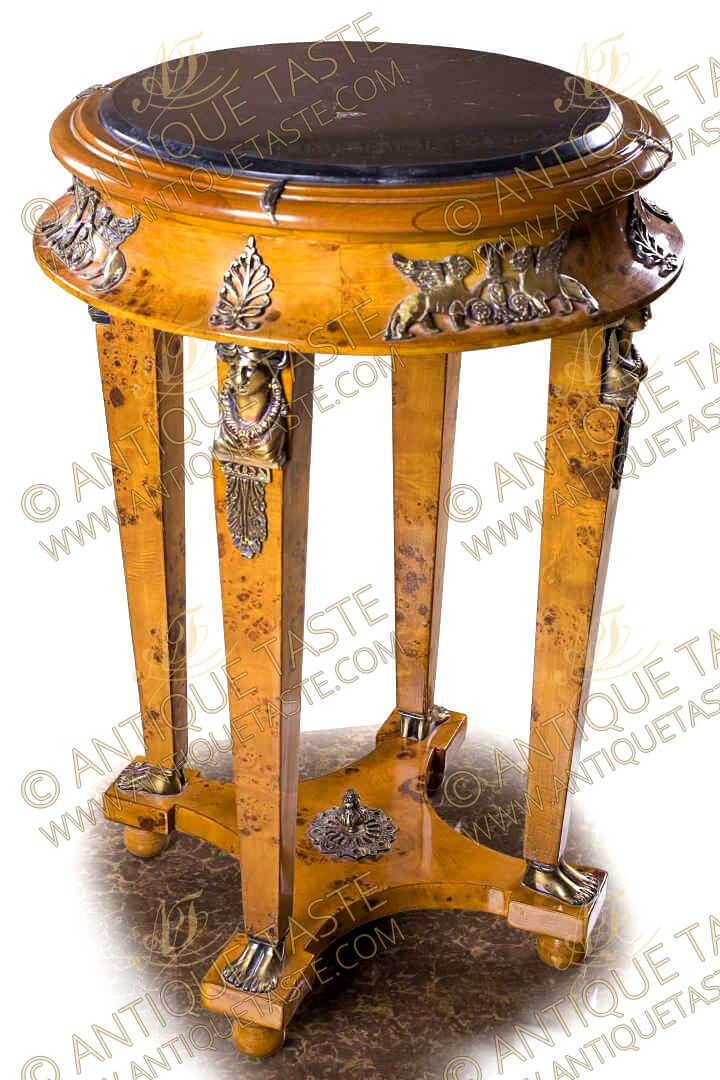 A fine French Empire style ormolu-mounted burl ash veneer inlaid side table, The inset beveled marble top with a frieze ornamented with a scattered leaf above a concave apron ornamented with winged mythological creatures and palemettes above four square tapered legs, Each leg is decorated by richly chased ormolu Caryatides in traditional attire and floral head dress, accented by foliate ormolu mount pendants and terminating in double human feet sabots, The supports connected with a tier concave sides stretcher centered by an ormolu foliate finial and raised on ball feet