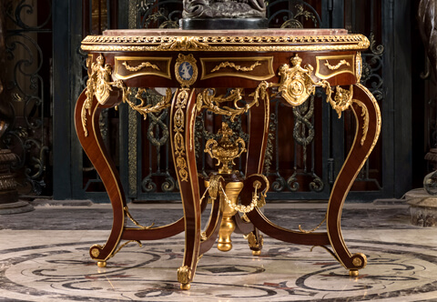 A stunning and most elegant French Louis XV style ormolu-mounted veneer inlaid Regal Center Table; marble topped, massively adorned with fine molded ormolu mounted of scrolling acanthus leaves, double ormolu trims, the apron is ornamented with the Royal Family Coat of Arms and Wedgwood jasperware plaques within ribbon-tied laurel wreath festoons; the bold cabriole legs on ball feet and connected by a rich stretcher centered by a reversed topie shaped finial surmounted by a fine ormolu urn or prosperity