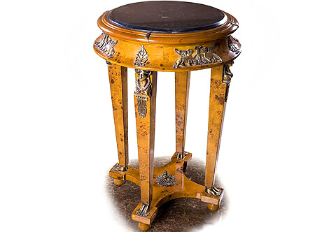 A fine French Empire style ormolu-mounted burl ash veneer inlaid side table, The inset beveled marble top with a frieze ornamented with a scattered leaf above a concave apron ornamented with winged mythological creatures and palemettes above four square tapered legs, Each leg is decorated by richly chased ormolu Caryatides in traditional attire and floral head dress, accented by foliate ormolu mount pendants and terminating in double human feet sabots, The supports connected with a tier concave sides stretcher centered by an ormolu foliate finial and raised on ball feet.