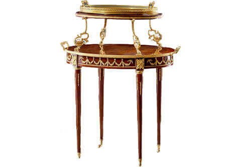 French Louis XVI style ormolu mounted two tier serving tea gueridon after the model by Francois-Linke late 19th century, The oval upper tier surmounted by an ormolu framed removable glass tray held to each side by a scrolled berry hung vine and laurel garland support. The lower quarter veneered top with molded surround applied with scrolling garlands, on fluted supports adorned with floral ormolu chandelles, headed by rosettes and terminated by gilt-ormolu wheel sabots